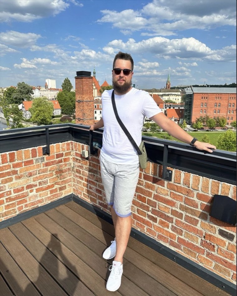 Szymon Lewandowski na tarasie z panoramą miasta w tle